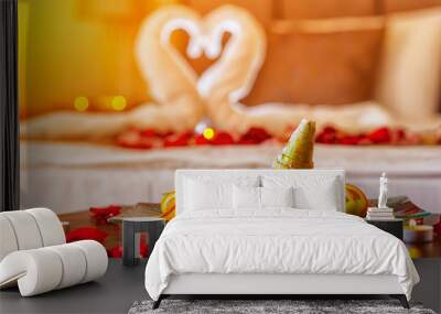 Romantic dinner for lovers: a table with a fruit plate and candles, in the background a bed decorated with swans of towels and rose petals Wall mural