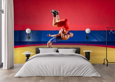 The concept of fair wrestling. Two greco-roman  wrestlers in red and blue uniform wrestling  on a yellow wrestling carpet in the gym Wall mural