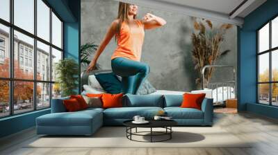 Young woman goes in for sports at home, training online. The  sporty woman does cardio workout, raises her legs high, steps in place in bedroom Wall mural