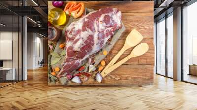 A raw leg of mutton on a bone lies on a piece of burlap , onions, garlic, pepper, salt,rosemary and vegetable oil on a wooden table. Sheep meat close-up.A fresh piece of mutton. The view from the top. Wall mural