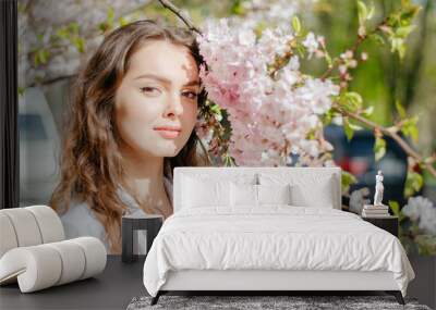 girl in a white shirt stands near the sakura in sunny spring weather Wall mural