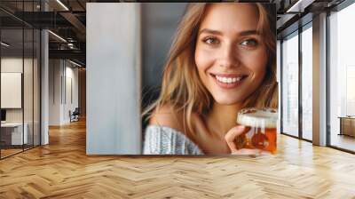 A happy Caucasian woman with wavy hair, holding a beer against a pink background Wall mural