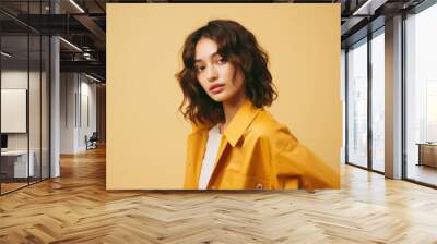 Portrait of cute Asian brunette in yellow jacket on yellow background. Wall mural