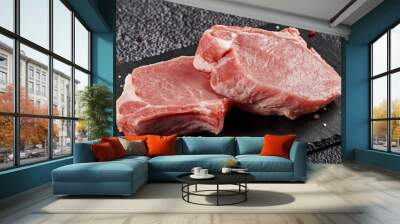 two pieces of raw pork meat with a bone for a steak on a black stone background Wall mural