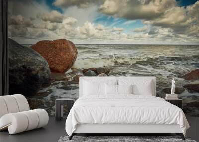 Stones at the beach with wave and nice blue sky with clouds Wall mural