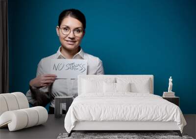 girl with glasses and a white shirt with a fake smile holds a piece of paper with the words no stress Wall mural