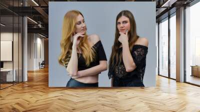 A concept portrait of two cute beautiful girls talking on a gray background in the studio Wall mural