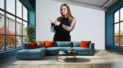 A photo of a pretty smiling brunette girl with excellent makeup in dark clothes is standing on a white background with emotions. Concept portrait for a banner. Wall mural