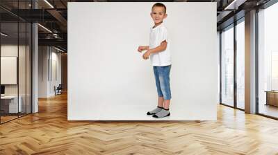 Full-length portrait on a white background of a cute boy child with Vitiligo disease - a violation of the color of the skin at the initial stage. White T-shirt, blue jeans. Wall mural