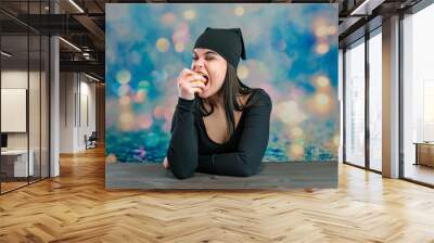 I'll tell you everything. Studio photo portrait of a cute young Caucasian brunette girl with an apple and a black dress looking straight into the camera on a colored background talking. Wall mural