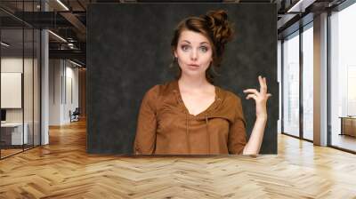 Portrait below breast over gray background of pretty young brunette woman in brown dress with beautiful hair. Standing in different poses, talking, showing with hands, demonstrating emotions. Wall mural