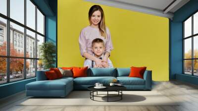 Portrait of a happy family: mom and a cute boy of 10 years of schoolboy on a yellow background in trousers and a shirt. Standing right in front of the camera, showing emotions, smile Wall mural