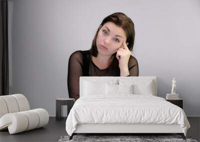 Portrait of a pretty beautiful fashionable adult girl with beautiful brunette hair in a black dress. Sits at the table directly in front of camera, talking demonstrating different poses and emotions Wall mural