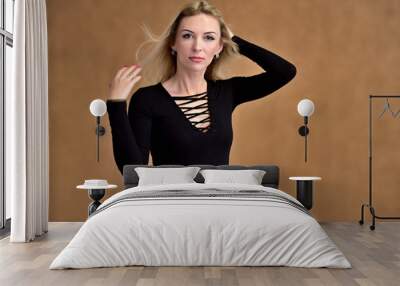 Studio portrait of a pretty blonde student girl with long hair in a black blouse on a beige background. Smiling at camera with emotions in various poses. Wall mural