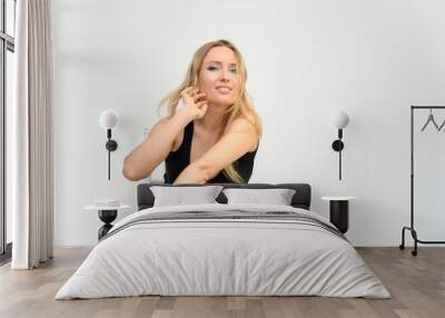 Studio waist-length photo portrait of a pretty beautiful young happy blonde woman with long hair on a white background in a black t-shirt and red trousers. Sits on a chair, smiles, shows emotions. Wall mural