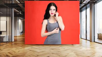 The concept of a beautiful female portrait with emotions. Portrait of a brunette girl with a smile with long hair with excellent makeup in a gray dress on a red background in different poses. Wall mural