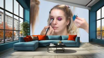 The work of a professional make-up artist, beautician, makes makeup on the face of a blonde girl with shadows on the eyes. Wall mural