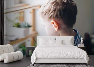 Caucasian boy watering from a yellow watering can home plants on the windowsill Wall mural