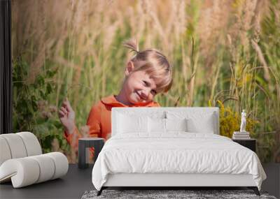 Cute little girl smiles looking at the camera and holds a bouquet of wildflowers Wall mural