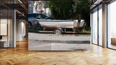 A white fishing boat loaded into a trailer stands in a parking space for cars. The old motorboat in the trailer is ready for transportation and fishing. Wall mural