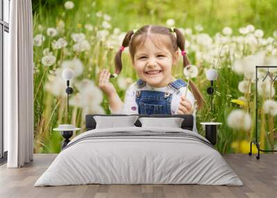 a beautiful cheerful funny girl with two tails sits on a field with dandelions and laughs Wall mural