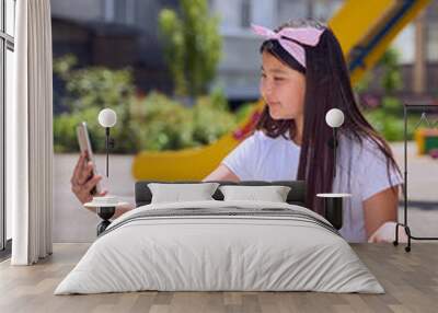 beautiful little Asian girl with black hair with a phone takes a selfie on the Playground Wall mural