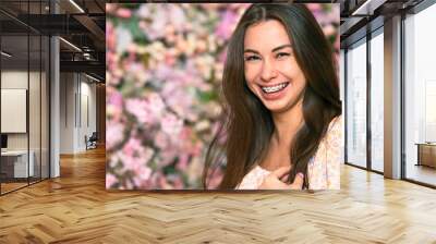 Young beautiful woman portrait. Female, girl smiles, smile with braces on a pink background with flowers. Copy space for billboard, Beauty and freshness of spring Wall mural