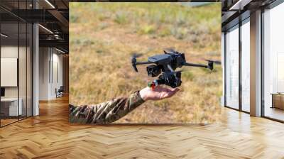 Soldiers launching a combat drone into flight. A soldier uses a drone for reconnaissance during a military operation. A soldier ties a grenade to blow up an enemy with a military drone. Wall mural