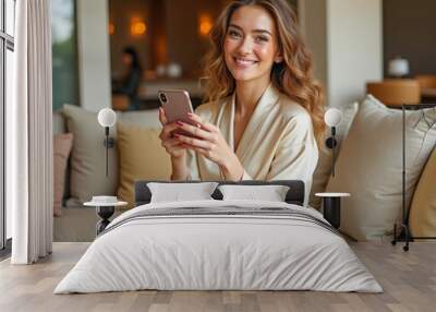 A beautiful girl in a bathrobe is typing on her phone and smiling Wall mural