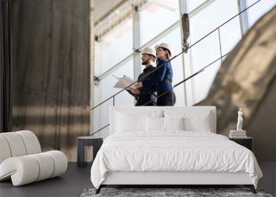 Two engineers, a man and a woman in construction helmets looking at a construction project. In white construction helmets standing on a construction bridge. Photographed from below. Wall mural