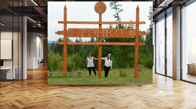 Two friends of an Asian Yakut stand under a wooden sign with the name of the village 