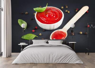 Bowl of ketchup and spoon of red tomato sauce on black kitchen table Wall mural