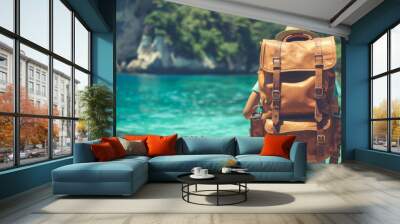 A person is standing on a beach with a brown backpack on. The backpack is large and has straps. The person is looking out at the ocean, which is blue and calm. Concept of relaxation and adventure Wall mural