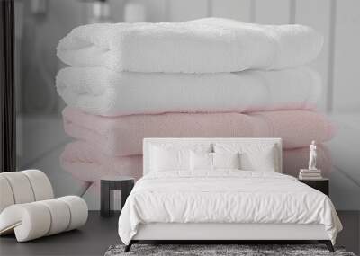 Three towels stacked on top of each other, one is pink and the other two are white. The towels are neatly folded and arranged on a wooden surface. Concept of order and cleanliness Wall mural