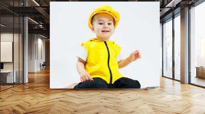 A little boy 2 years old in a builder's suit on a white background. A child in a plastic helmet and plastic tools. Plastic children's toys. Wall mural