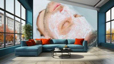 A man with a mask in a beauty salon. Men's face care concept. A beautician puts a mask on a client's face in a spa center. Male cosmetology. Wall mural