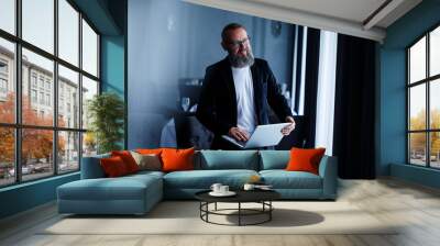 An adult businessman with a beard in glasses sits with a laptop on his lap and works. The director makes a schedule for the workflow Wall mural