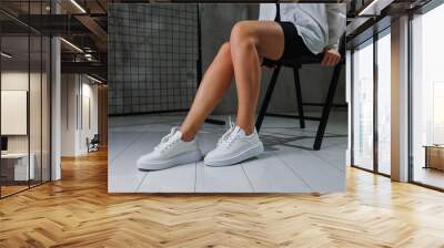 Beautiful female legs in leather white casual sneakers. Women's legs with fashionable shoes. Casual white women's shoes Wall mural