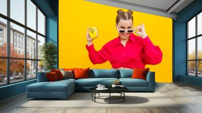 Cheerful pregnant woman holding a sweet yellow donut in her hand on a yellow background. Expecting a child, pregnancy and motherhood. The concept of healthy and unhealthy food, diet. Junk food Wall mural