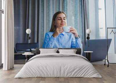 Portrait of cheerful woman in classic glasses smiling in free time in cafe with coffee, positive european woman in blue shirt, desk with laptop, remote work Wall mural