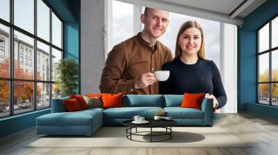 Stylish young couple in love in front of large panoramic windows. Young woman and man stand near a large window Wall mural