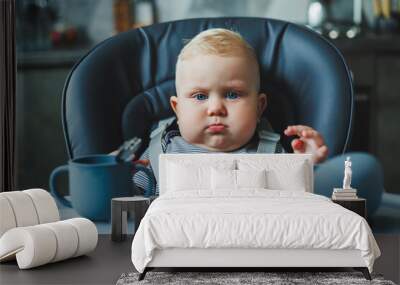 The baby sits in a high chair and eats from silicone dishes. Utensils for feeding babies. Wall mural