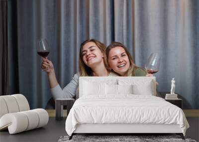 two girls of European appearance with blond hair are sitting at the table, drinking wine and laughing, relaxing at home, alcohol Wall mural