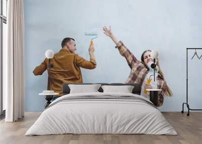 Young married couple in love in shirts and jeans doing renovations, renewing painting walls with a roller, preparing to move into a new house, selective focus Wall mural