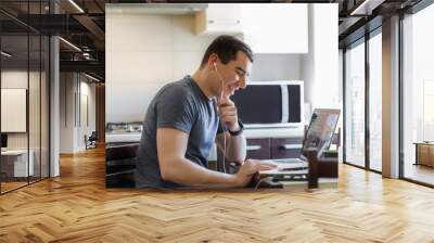 A young guy works remotely at home at a computer in the kitchen, flipping through a diary Wall mural