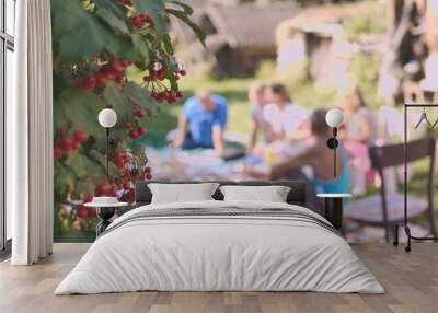 A family picnic of adults in the countryside against the backdrop of a red berry tree. Wall mural