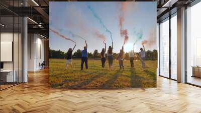 A group of friends spraying multi-colored smoke at sunset. Wall mural