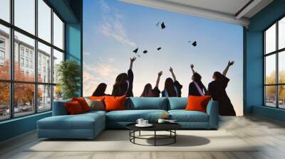 Silhouettes of graduates toss their caps at sunset. Wall mural