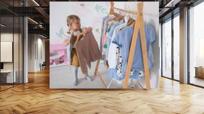 A little girl chooses clothes and puts things in order in the room, a child tries on dresses in a bright children's room Wall mural