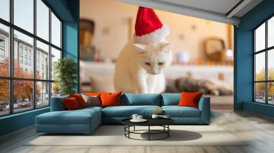 Cute cat in Santa Claus hat against blurred Christmas lights. Wall mural